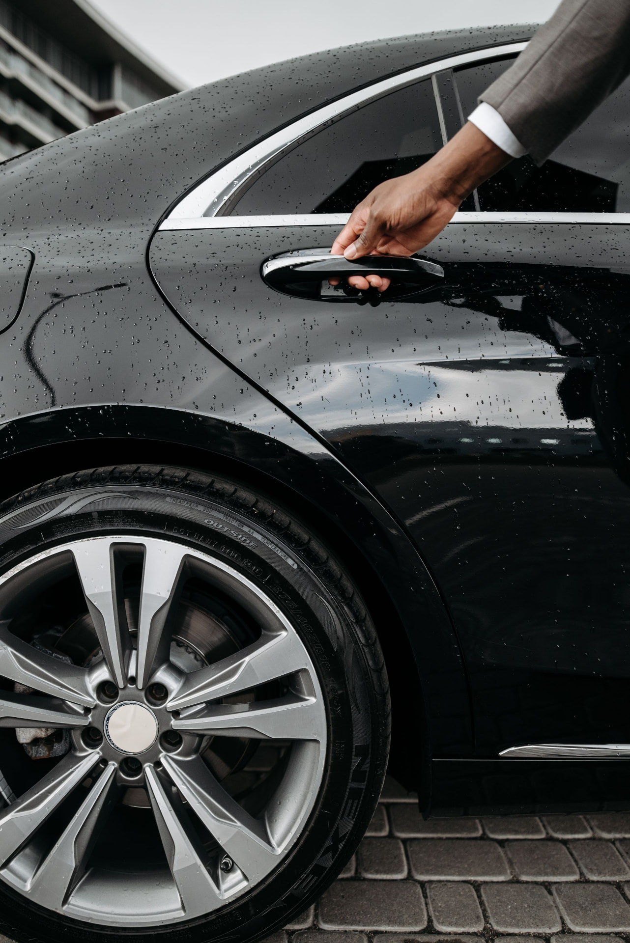 Close-up of a chauffeur's hand opening the door of a rain-beaded black luxury car