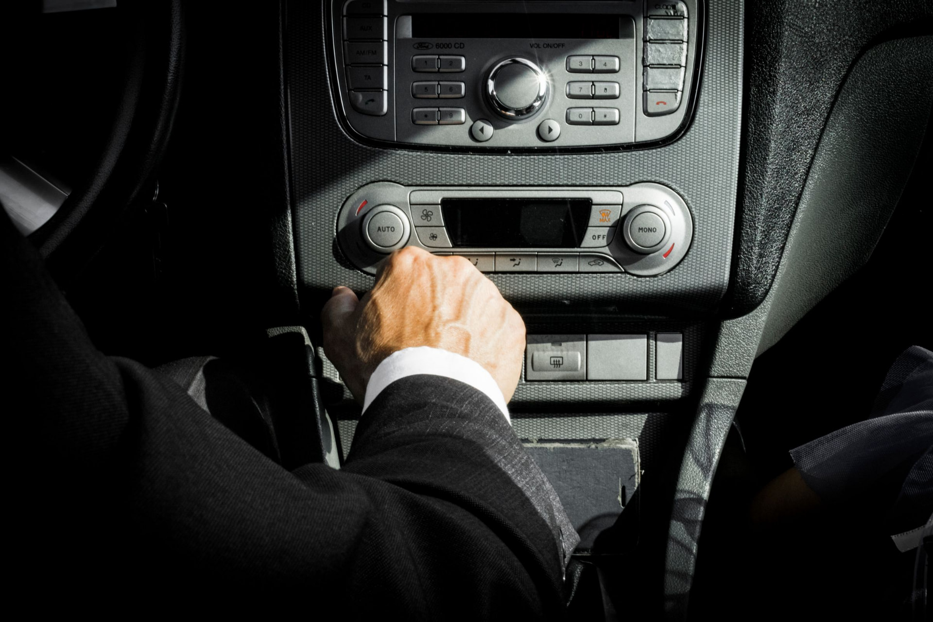 Suited passenger's hand on the gear selector inside a dark, quiet luxury car cabin